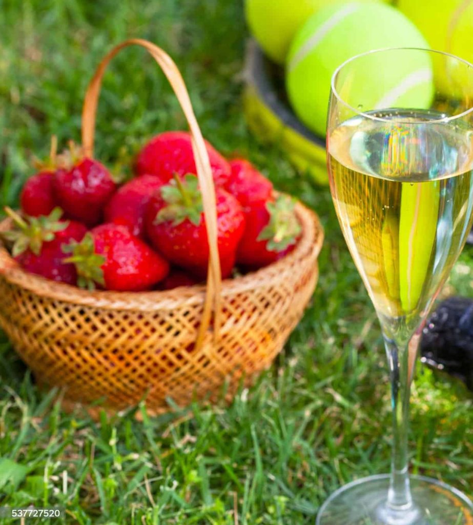 strawberries, champagne and tennis balls on racket in the grass
