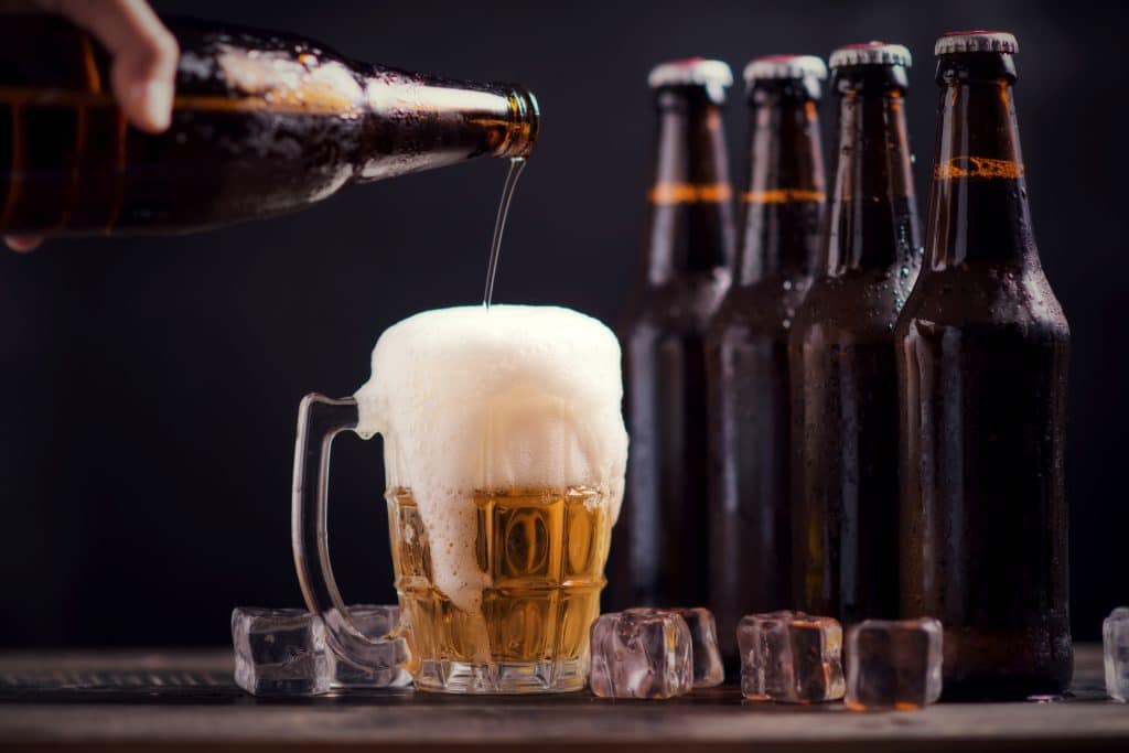 glass bottles of beer with glass and ice on dark background