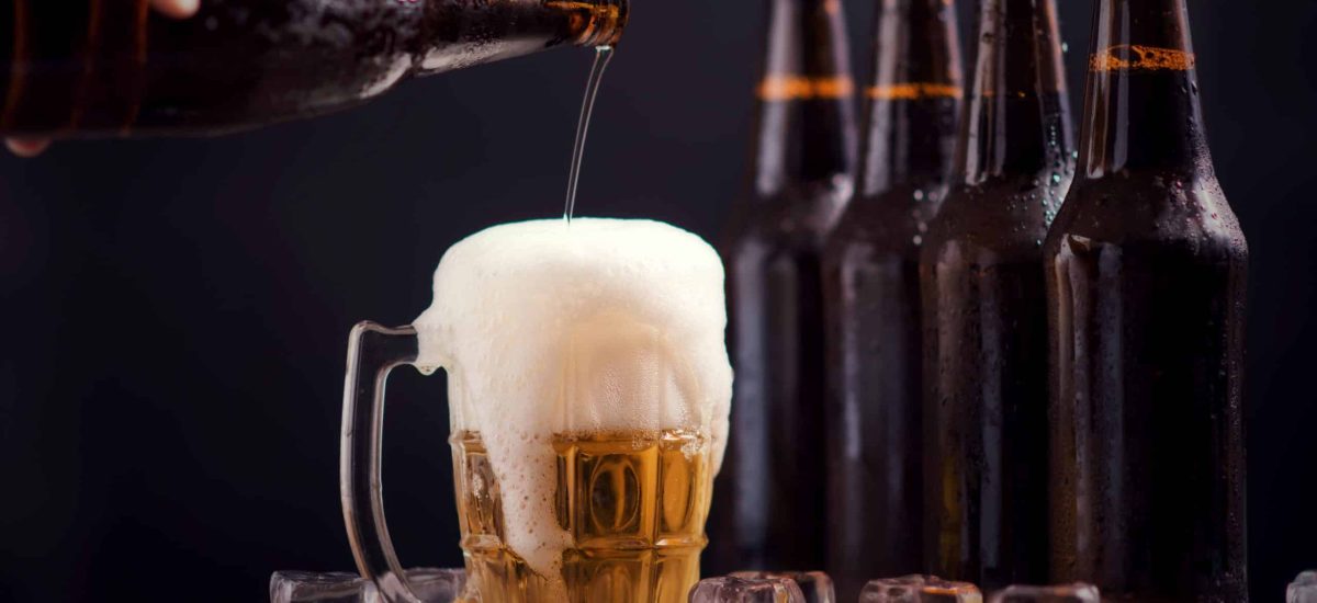 glass bottles of beer with glass and ice on dark background